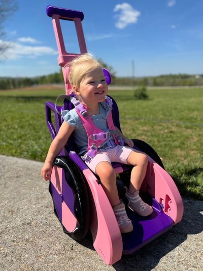 Girl is shown using a pink and purple Toddler Mobility Trainer
